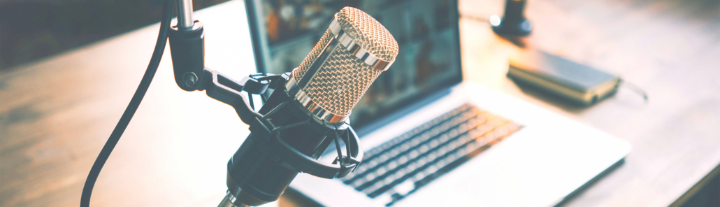Mikrofon in einem Raum, während im Hintergrund Podcasts auf einem Notebook zu sehen sind